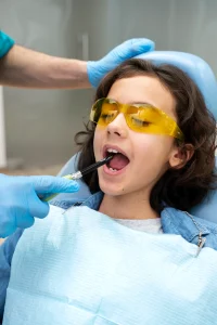 Pedodontics A child wearing yellow glasses is being treated by a dentist.