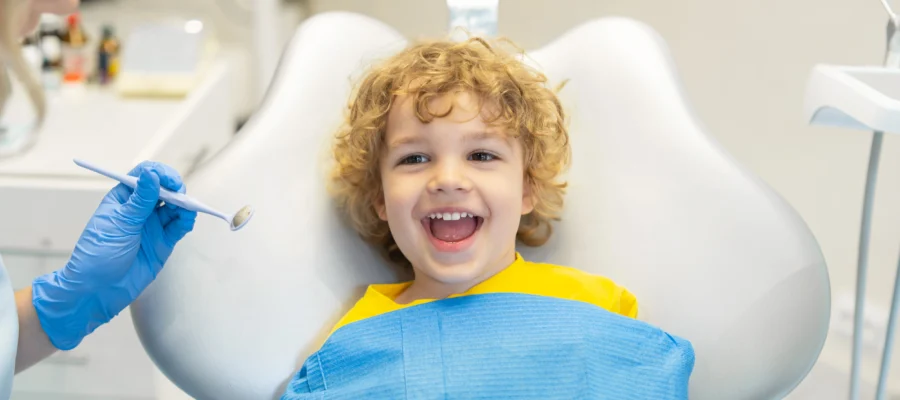 Gülümseyen bir çocuk diş hekimi koltuğunda oturuyor.